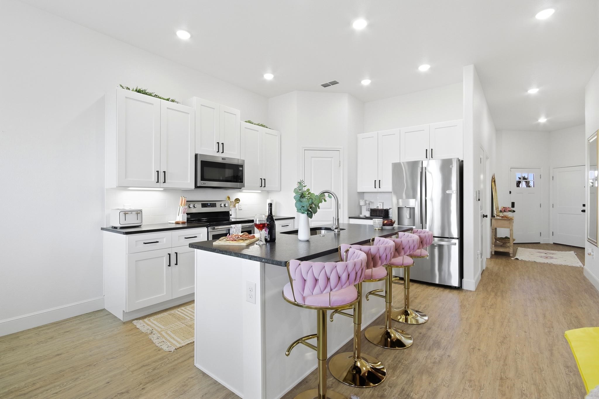 Modern kitchen with a dark island, stainless steel appliances, and pink upholstered bar stools.