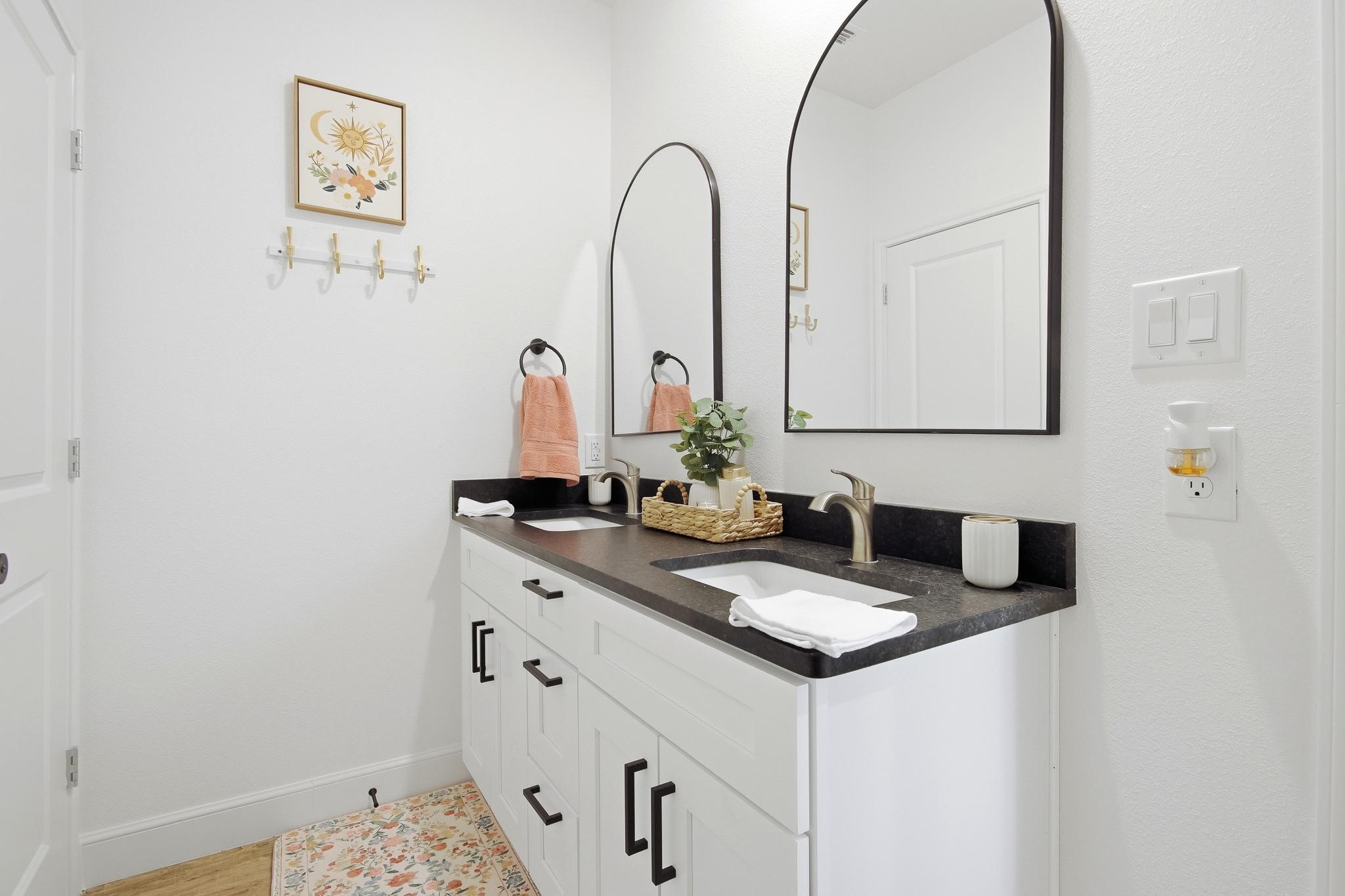 Bathroom with a double-sink vanity, dark countertop, arched mirrors, and peach towels.