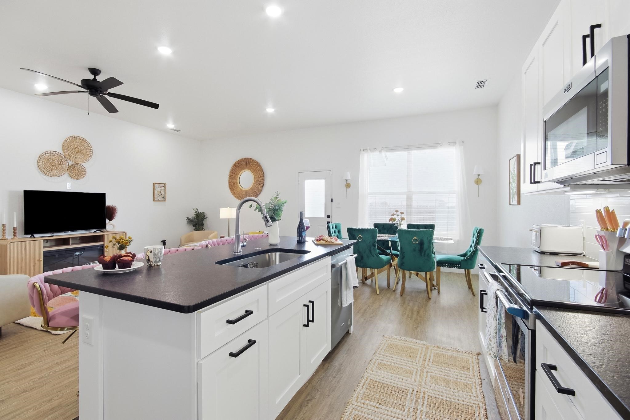Open-plan kitchen with a large island, white cabinetry, and teal dining chairs.
