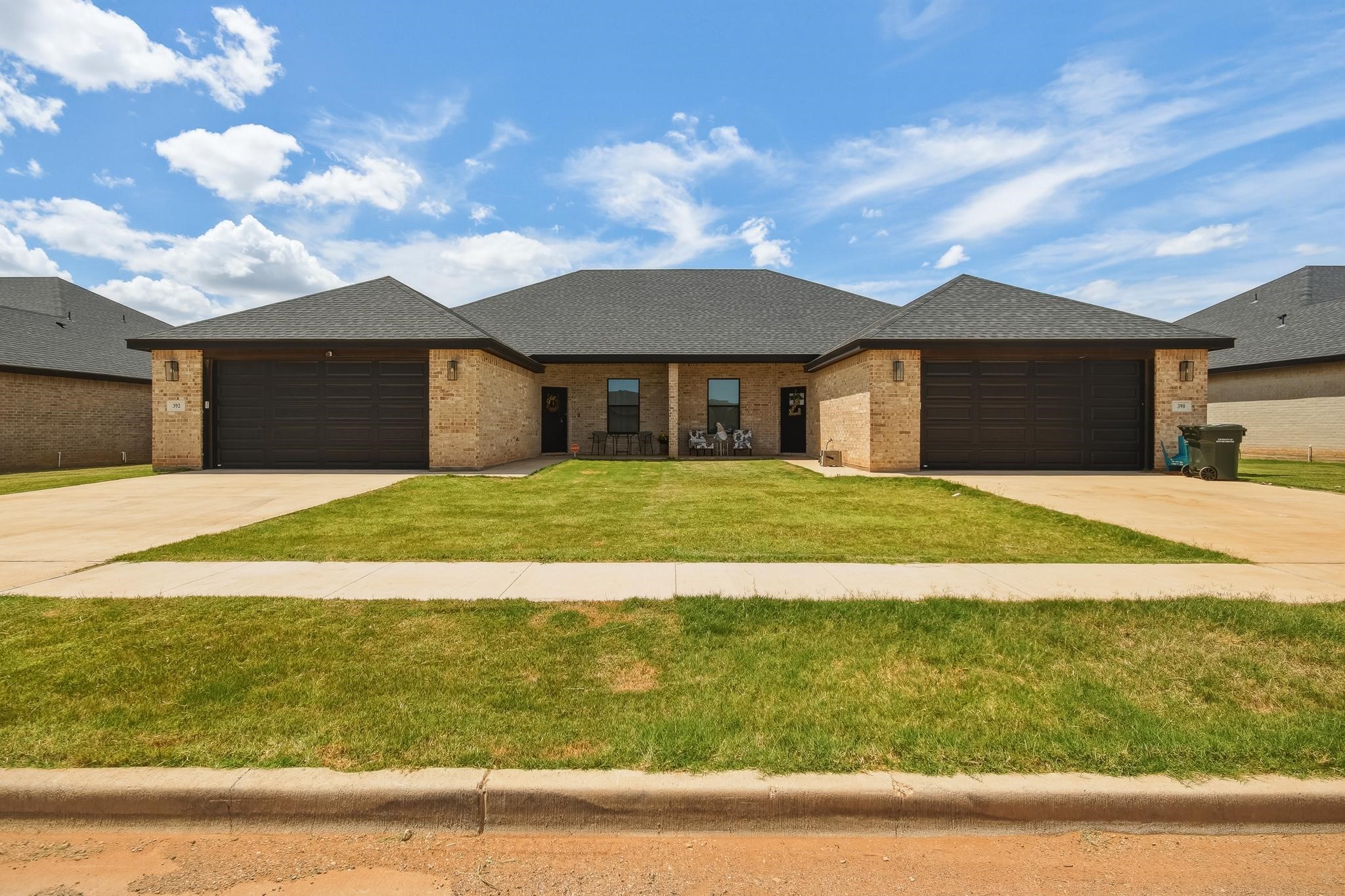 Two adjoining brick homes with separate double garages and driveways, viewed from across the lawn.