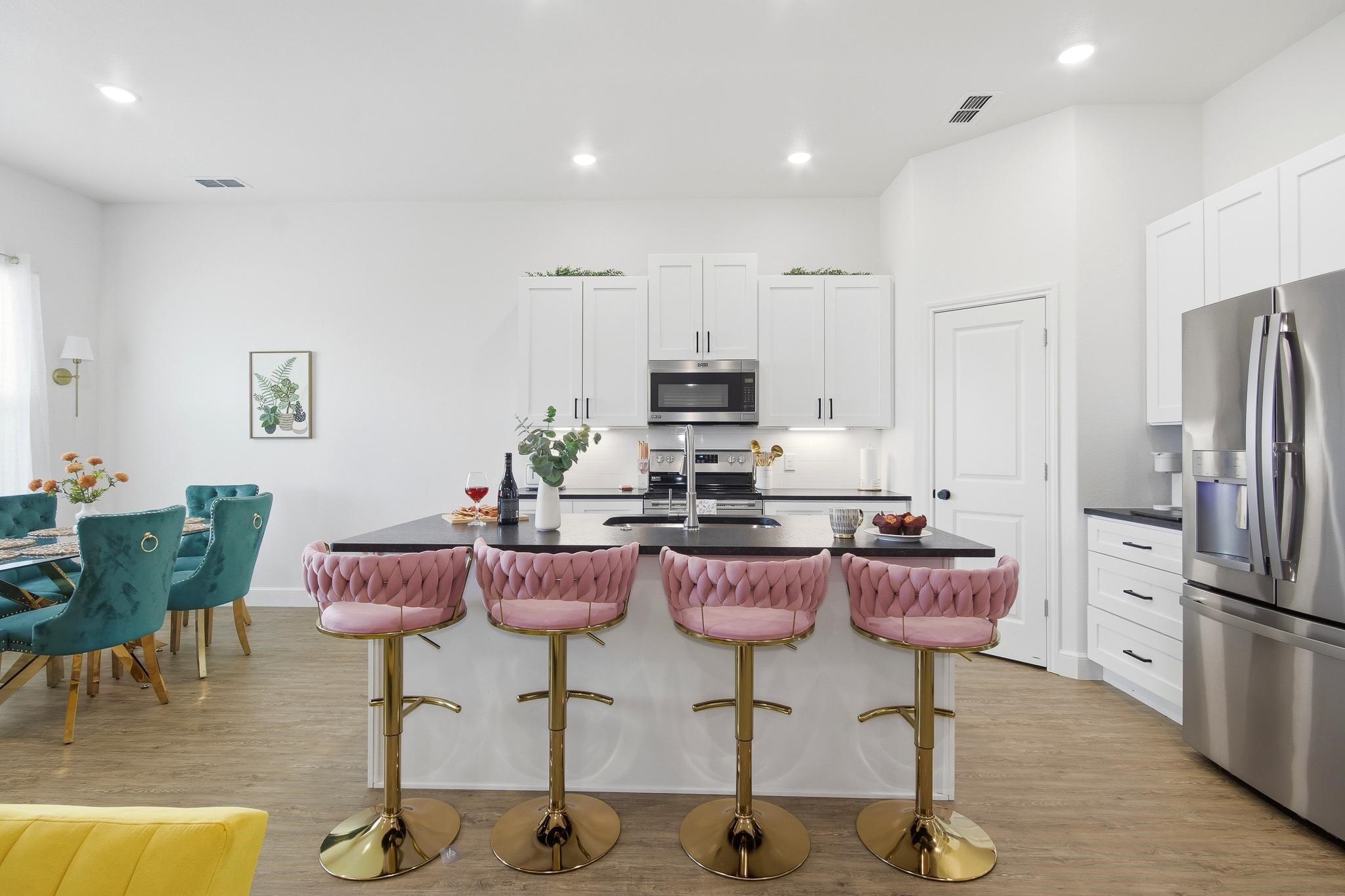 Kitchen with a dark island, four pink bar stools, white cabinets, and stainless steel appliances.