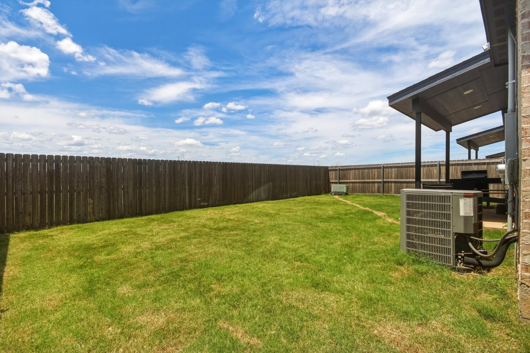 Fenced grassy backyard with a covered patio and grill beside the house.