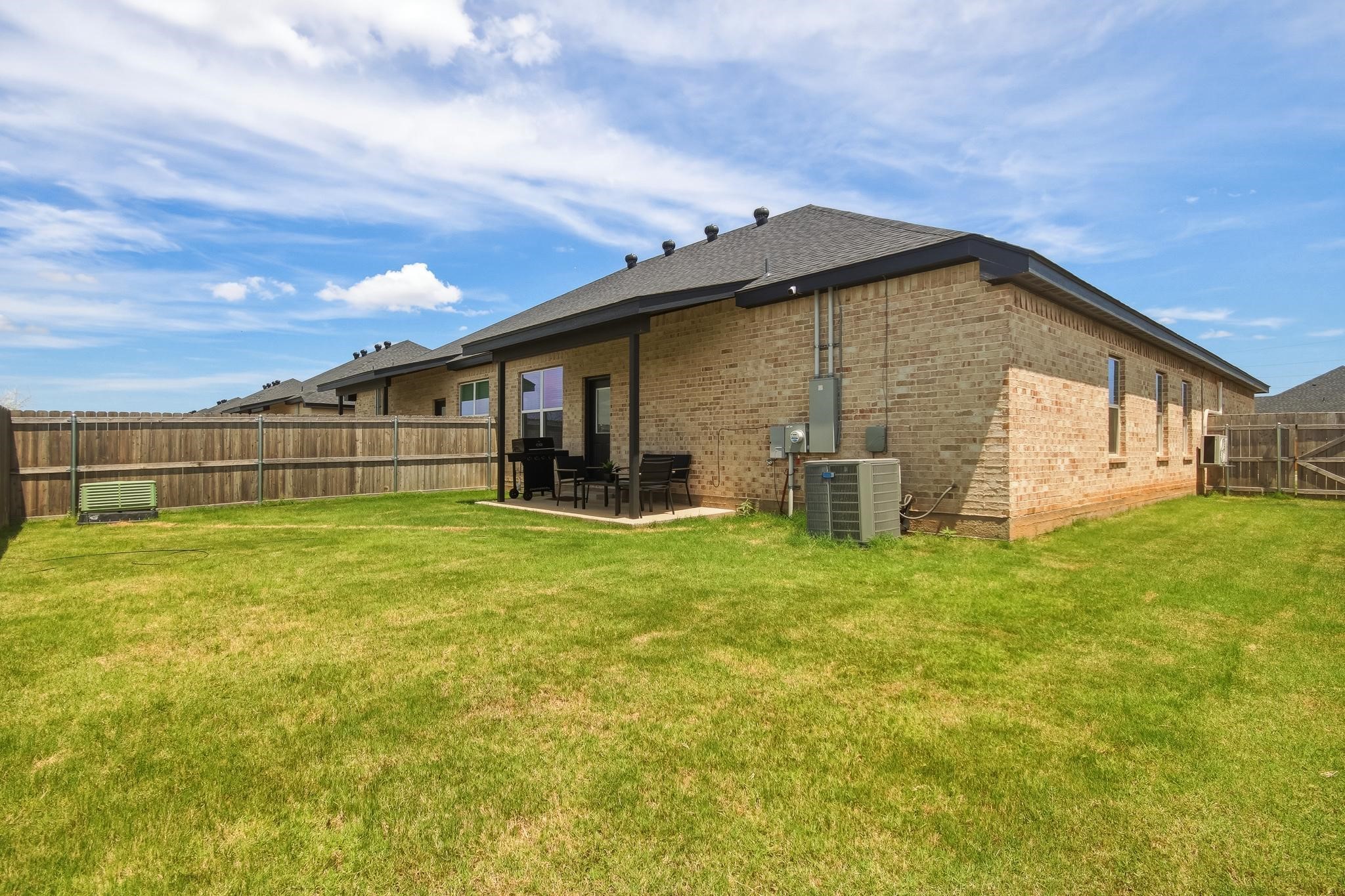 Brick home with a covered patio and grill overlooking a fenced backyard lawn.