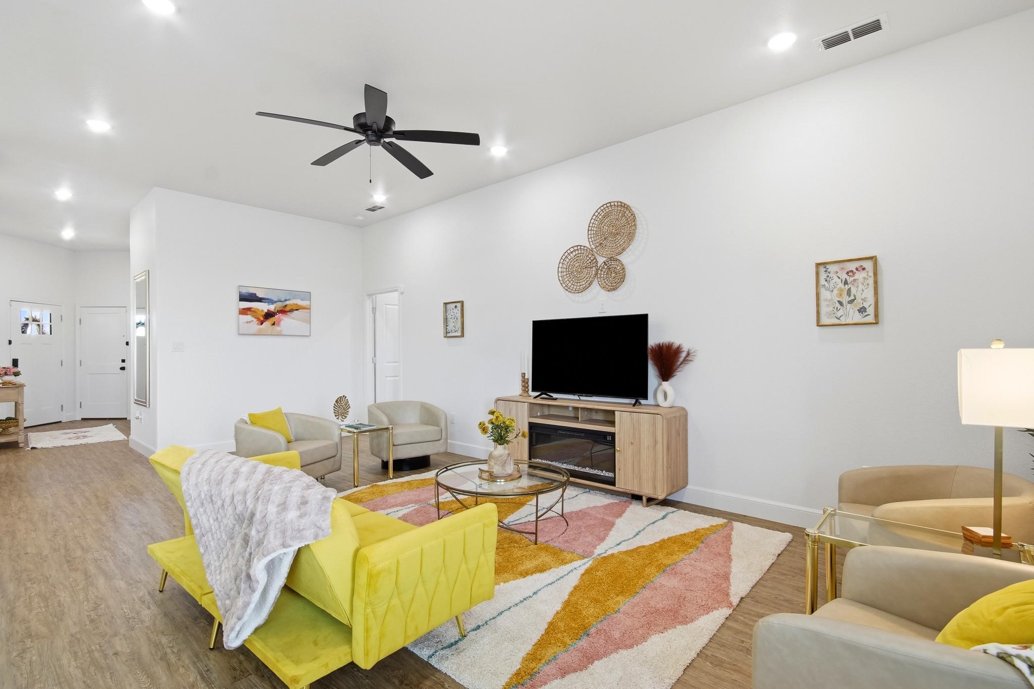 Staged living room with a bright yellow sofa, colorful rug, and TV above an electric fireplace.