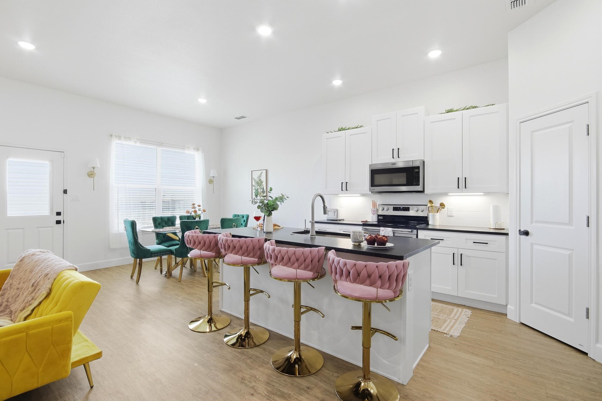 Open kitchen with black island, pink bar stools, and teal dining chairs.