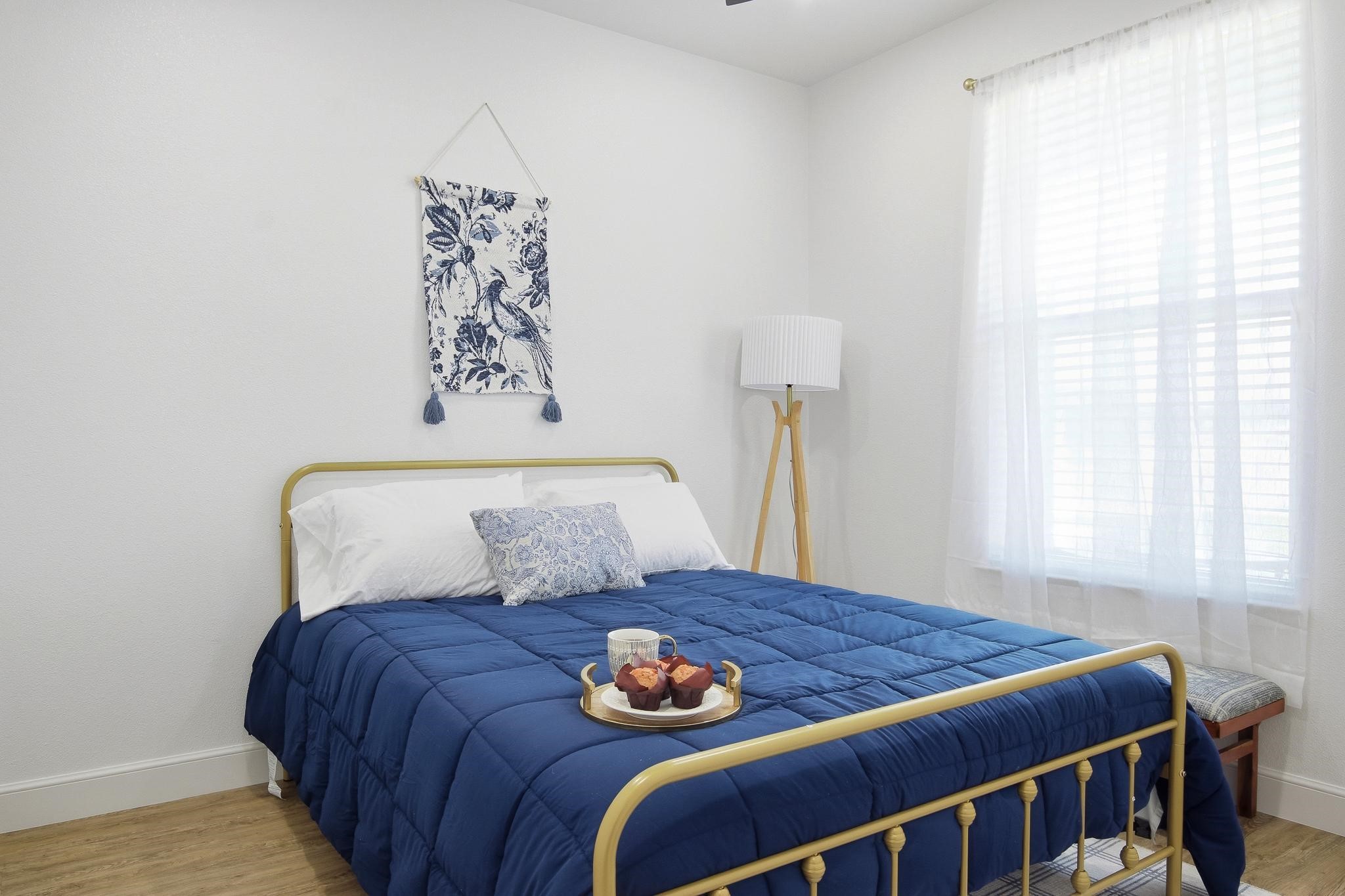 Staged bedroom with a navy quilt on a brass-tone bed and a tray of muffins.