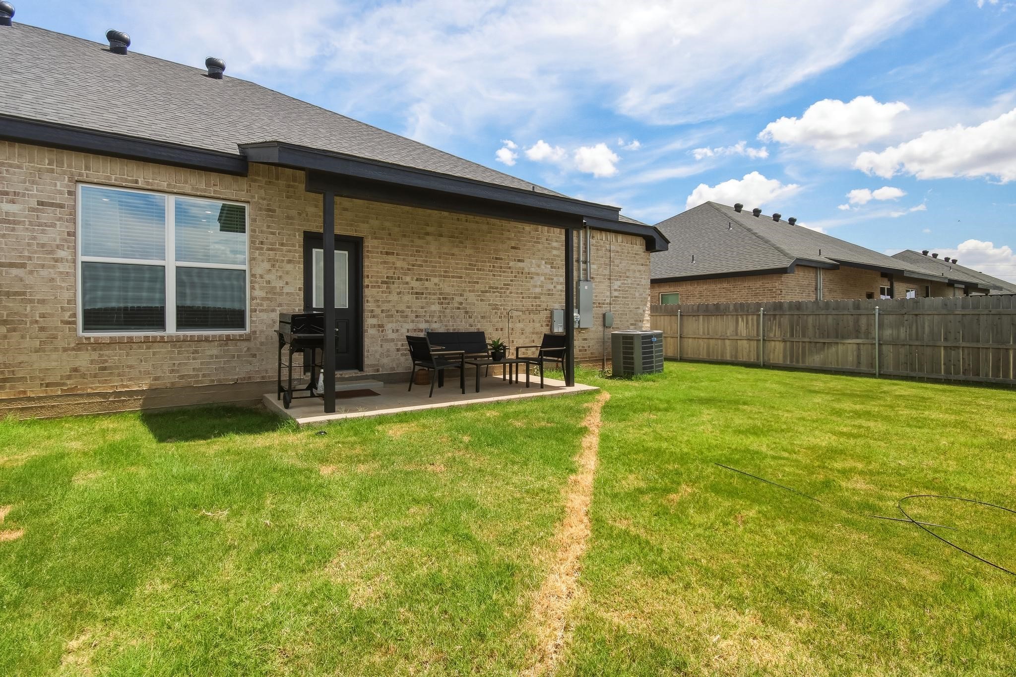 Brick home’s fenced backyard with covered patio seating and a broad lawn.