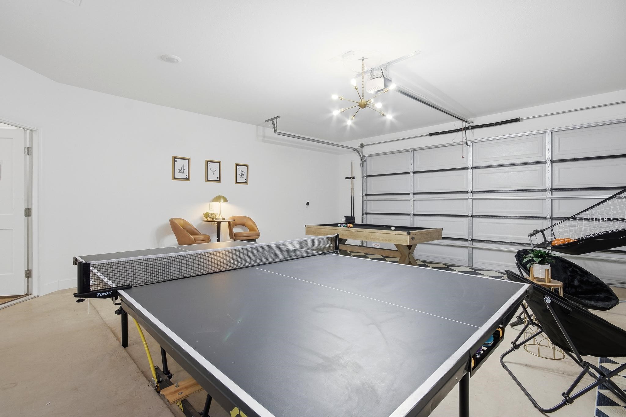 Furnished garage game room with a ping-pong table, pool table, and closed garage door.