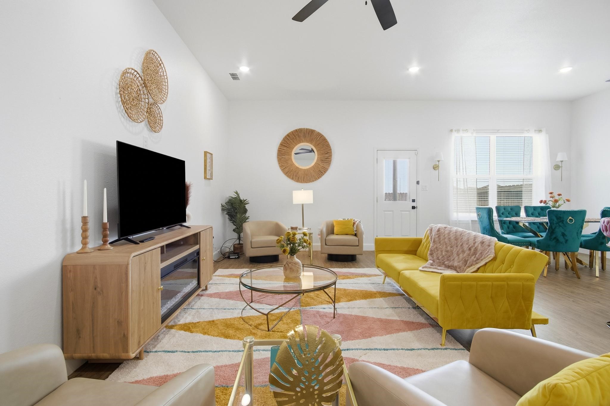 Staged living room with a yellow sofa, teal dining chairs, and a colorful geometric rug.