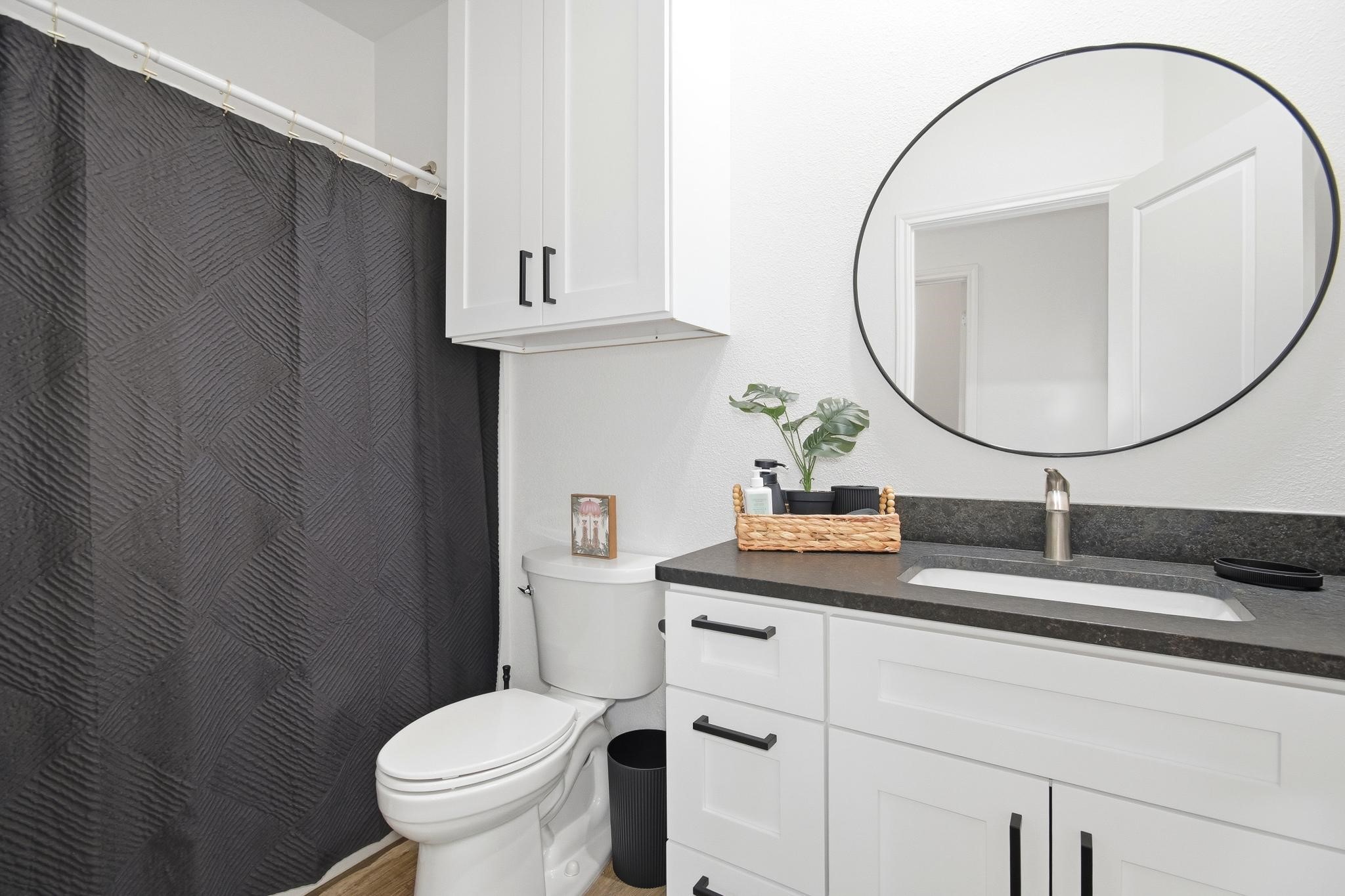 Bathroom with a white vanity, oval mirror, and charcoal geometric-patterned shower curtain.
