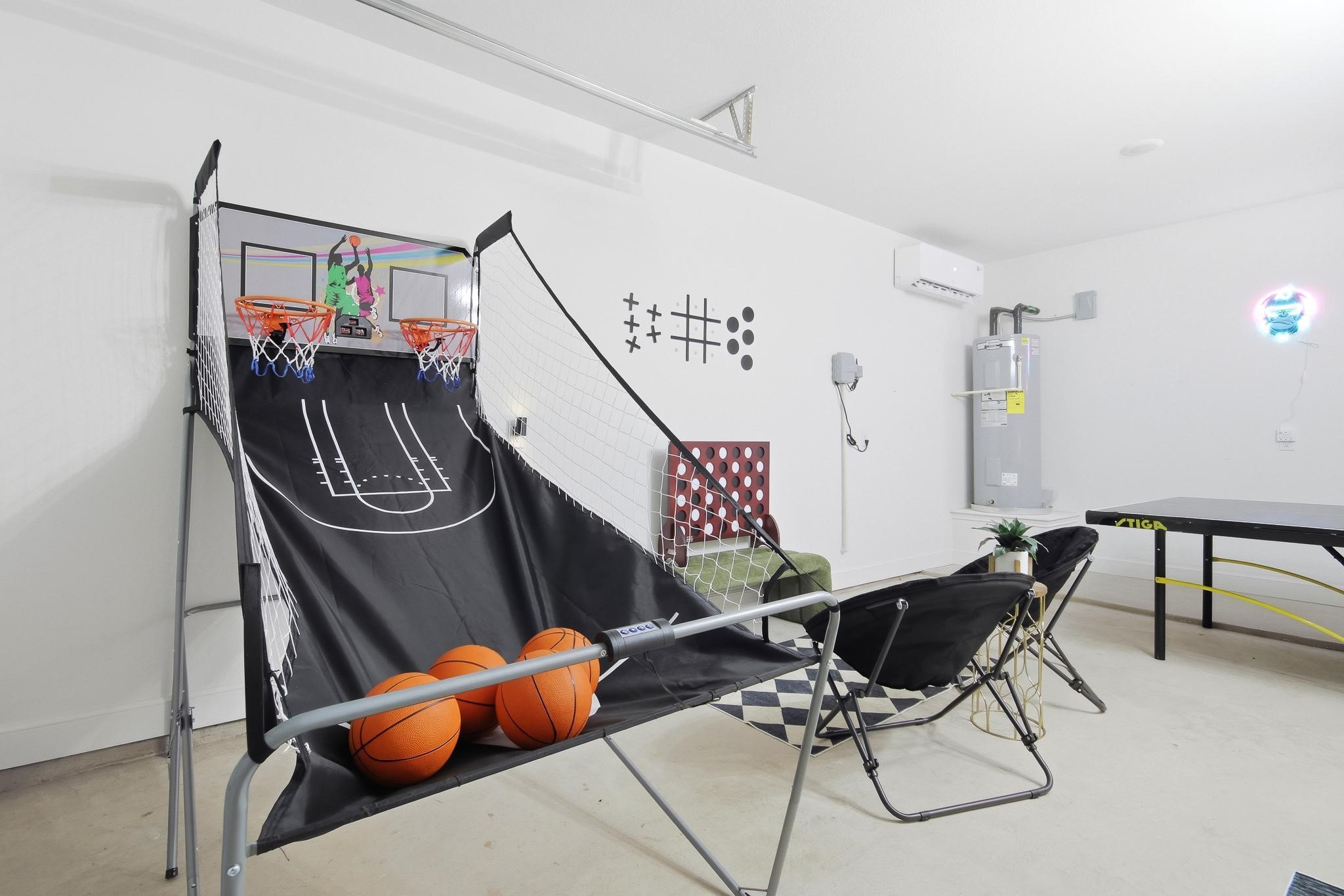 Garage game room with a basketball arcade game, ping-pong table, and folding lounge chairs.