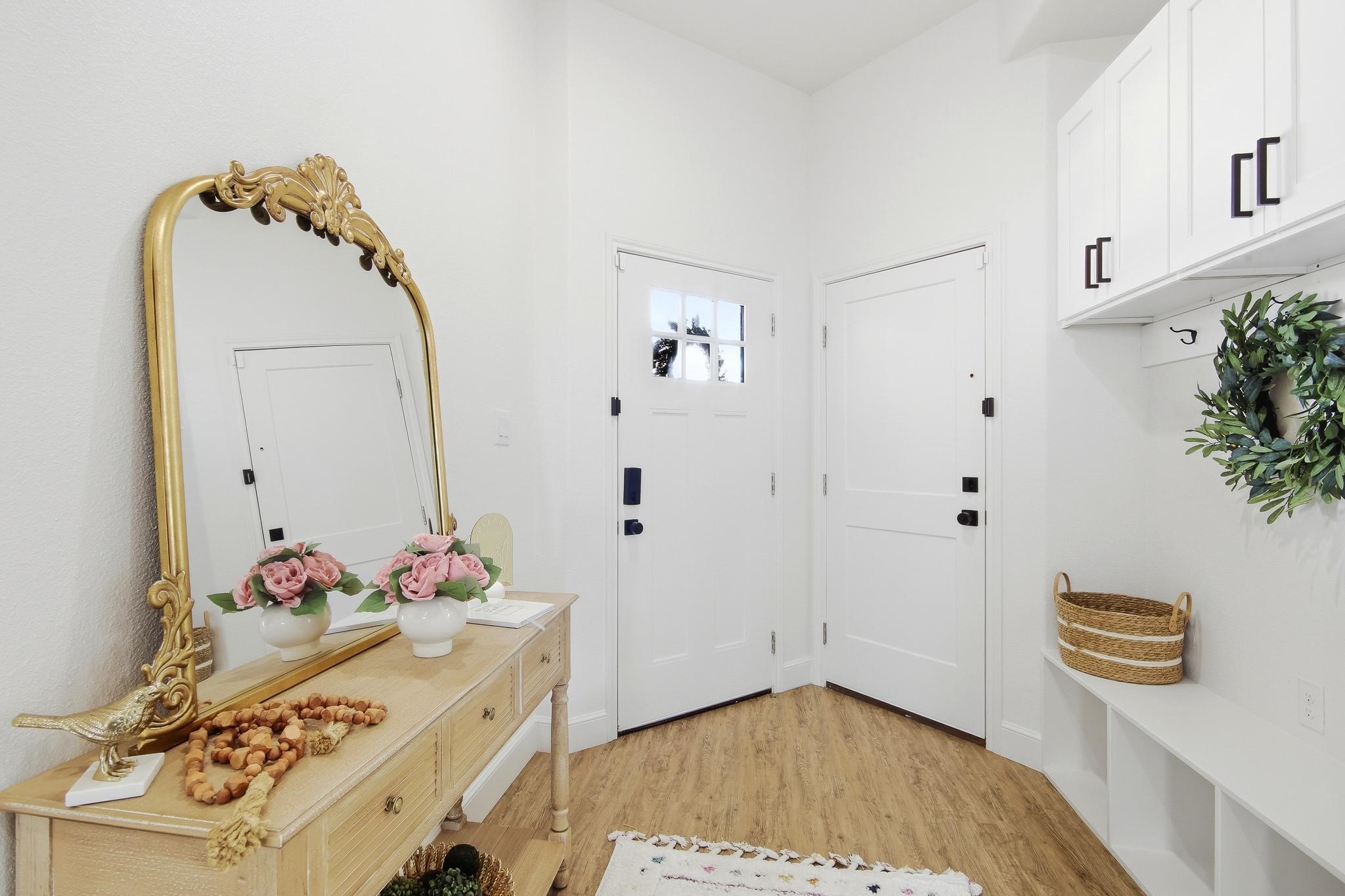 Furnished entryway with an ornate gold mirror, console table, built-in storage, and two white doors.