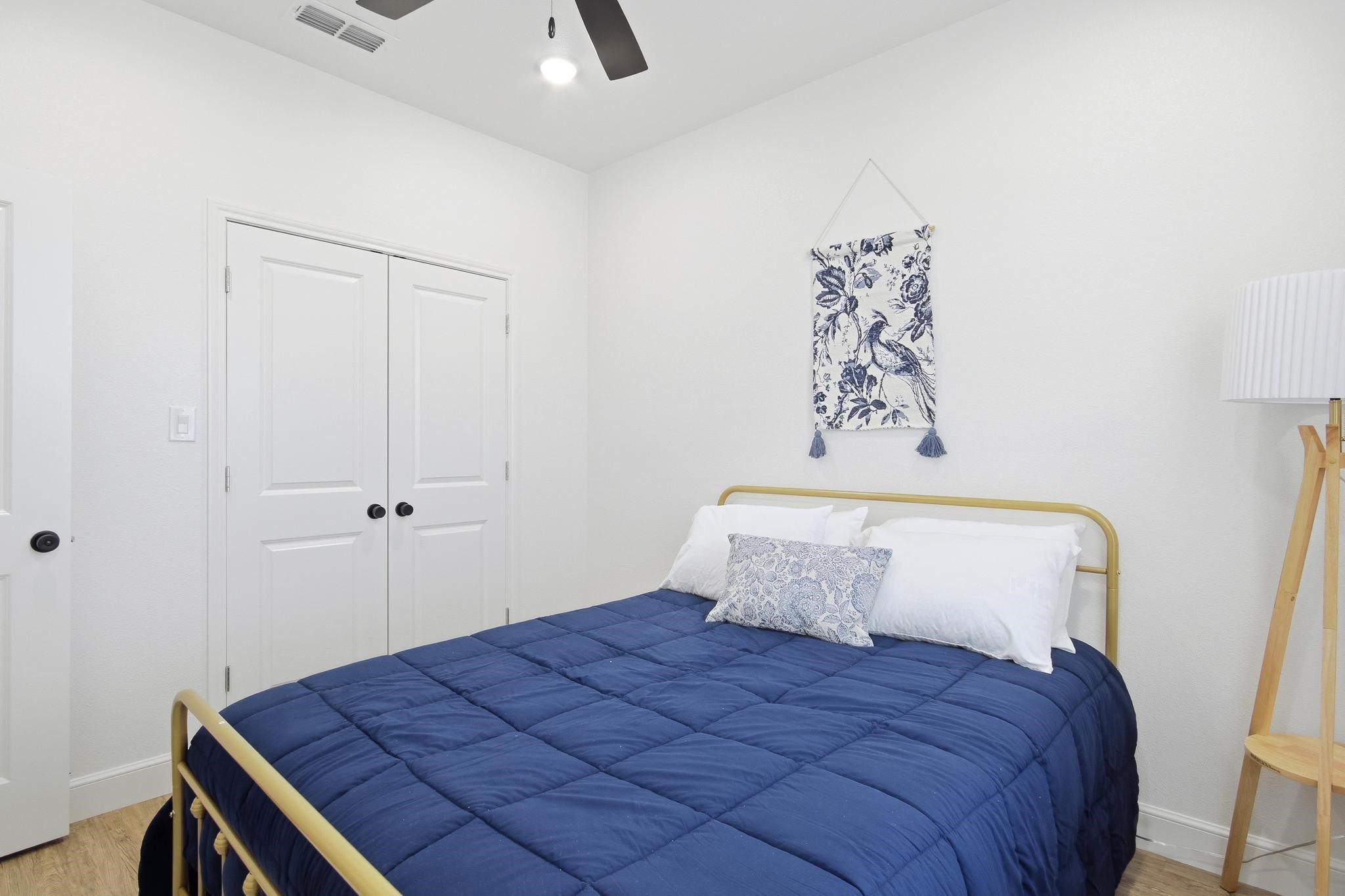 Staged bedroom with a navy quilt, brass bed frame, and bird-patterned wall hanging.