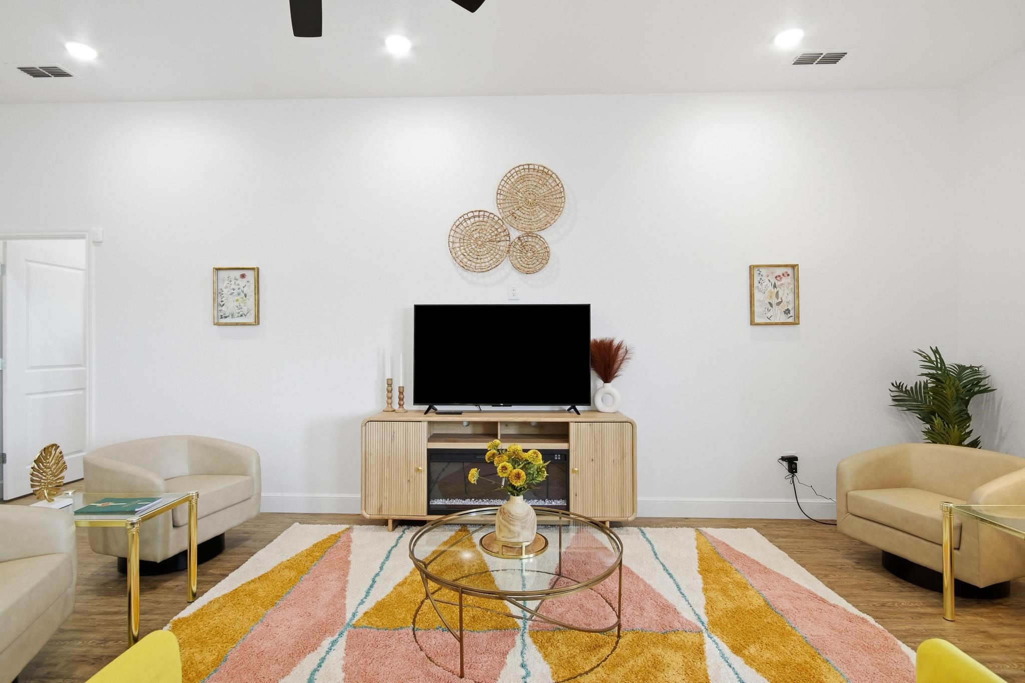 Staged living room with a TV above a fireplace and a colorful geometric rug.