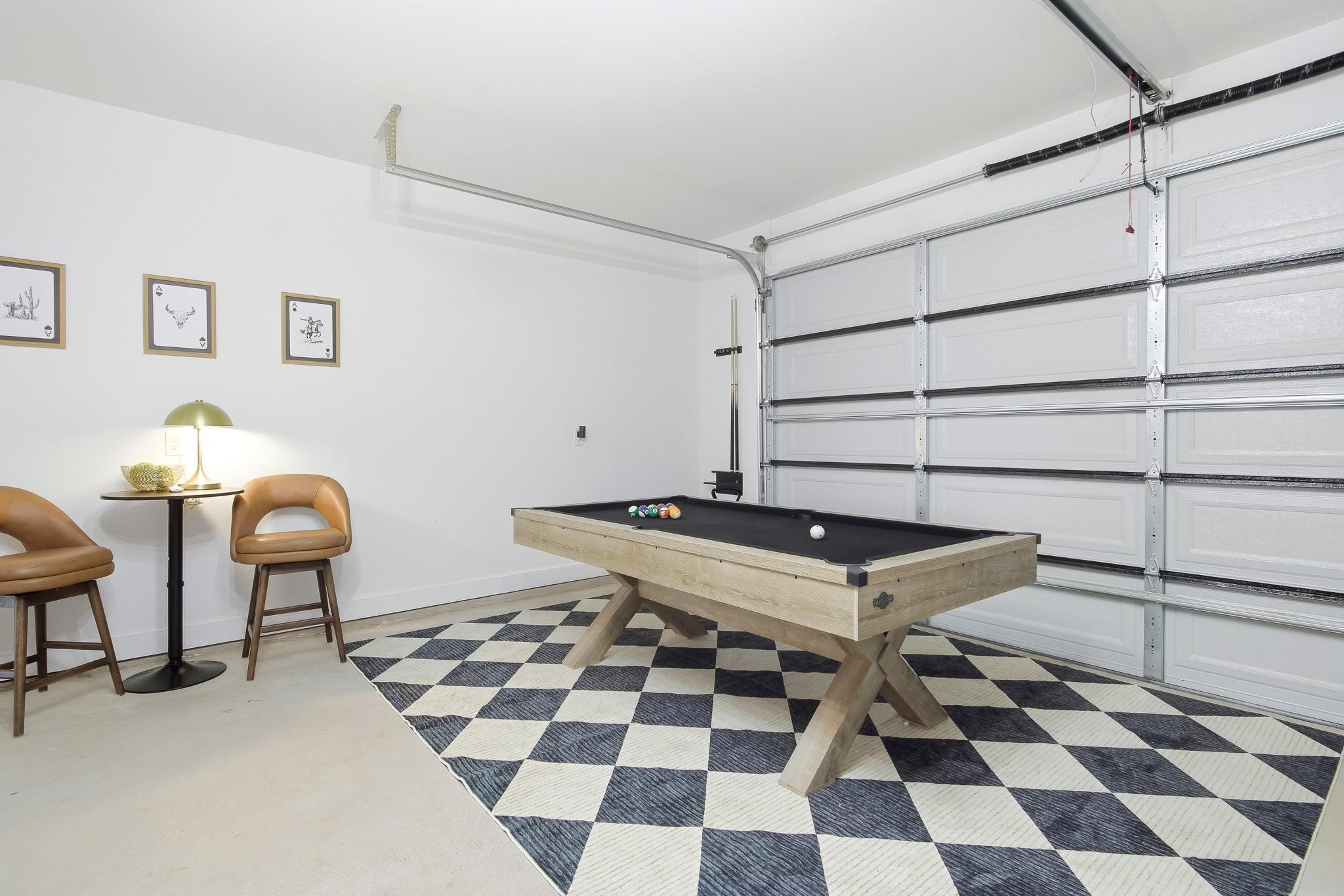 Game room with a pool table, checkerboard rug, tan chairs, and closed garage door.