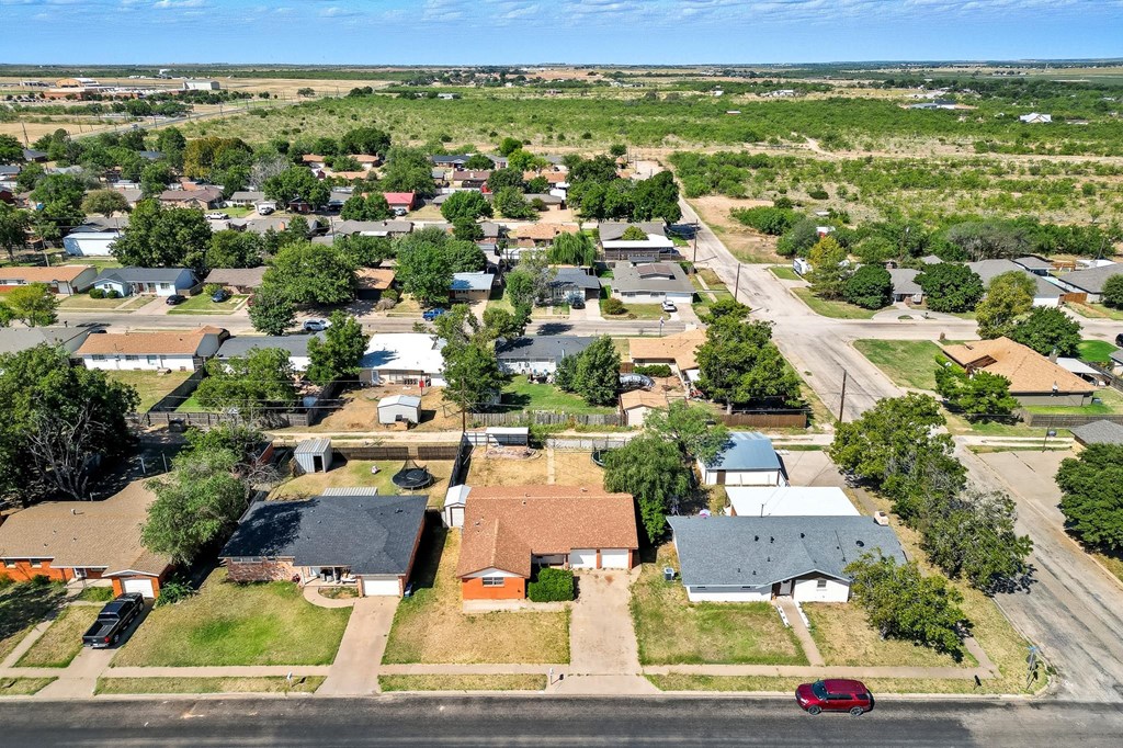 Aerial view of a brick home among single-story houses, with open land beyond the neighborhood.
