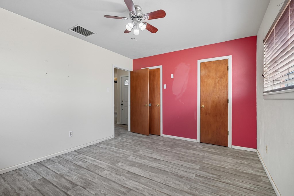 Vacant room with gray plank flooring, red accent wall, ceiling fan, and window blinds.