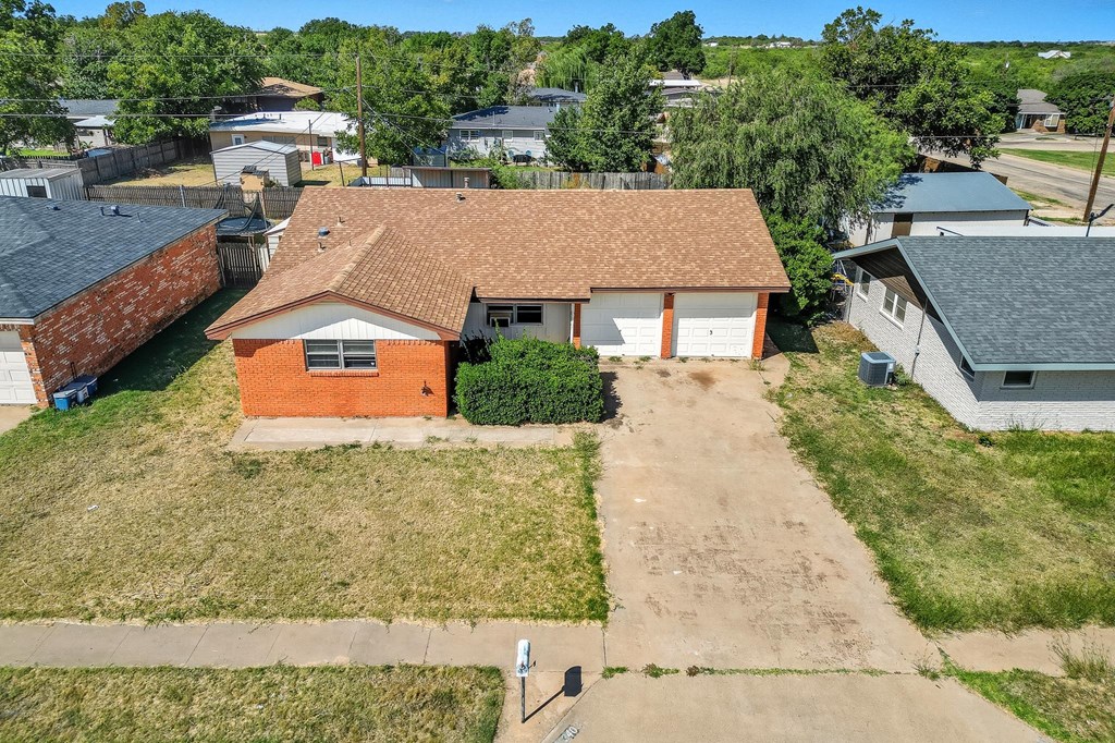 Aerial view of a red brick house with two garage doors and a long driveway.