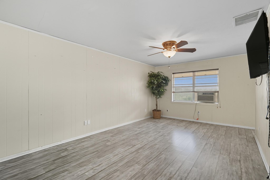 Empty room with gray wood-look flooring, a ceiling fan, window blinds, and a wall-mounted television.
