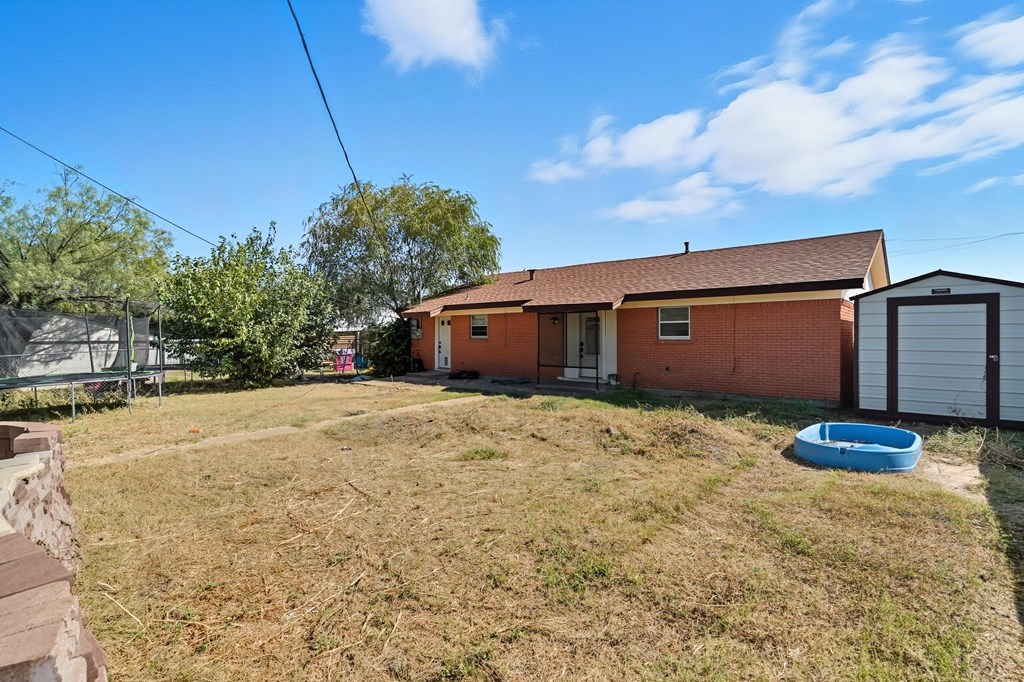 Brick house and storage shed behind a dry grassy yard with a small blue pool.