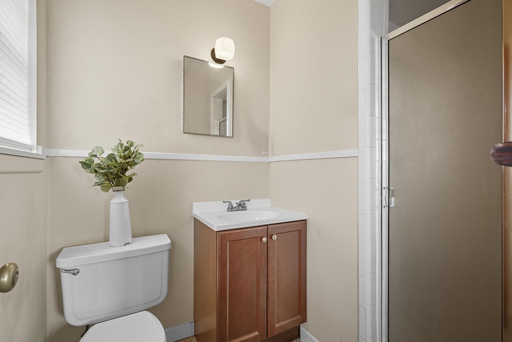 Bathroom with a brown wood vanity, glass shower enclosure, and vase of greenery on the toilet tank.
