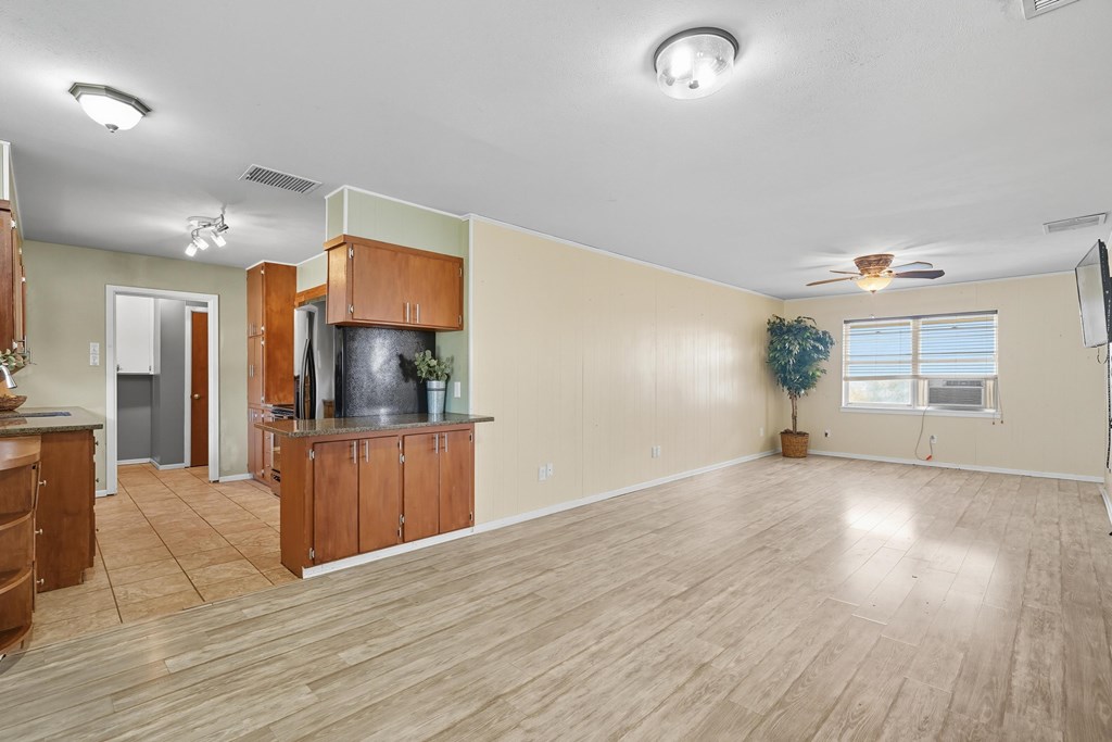 Unfurnished living area with wood-look floors, adjoining kitchen, and window air conditioner.