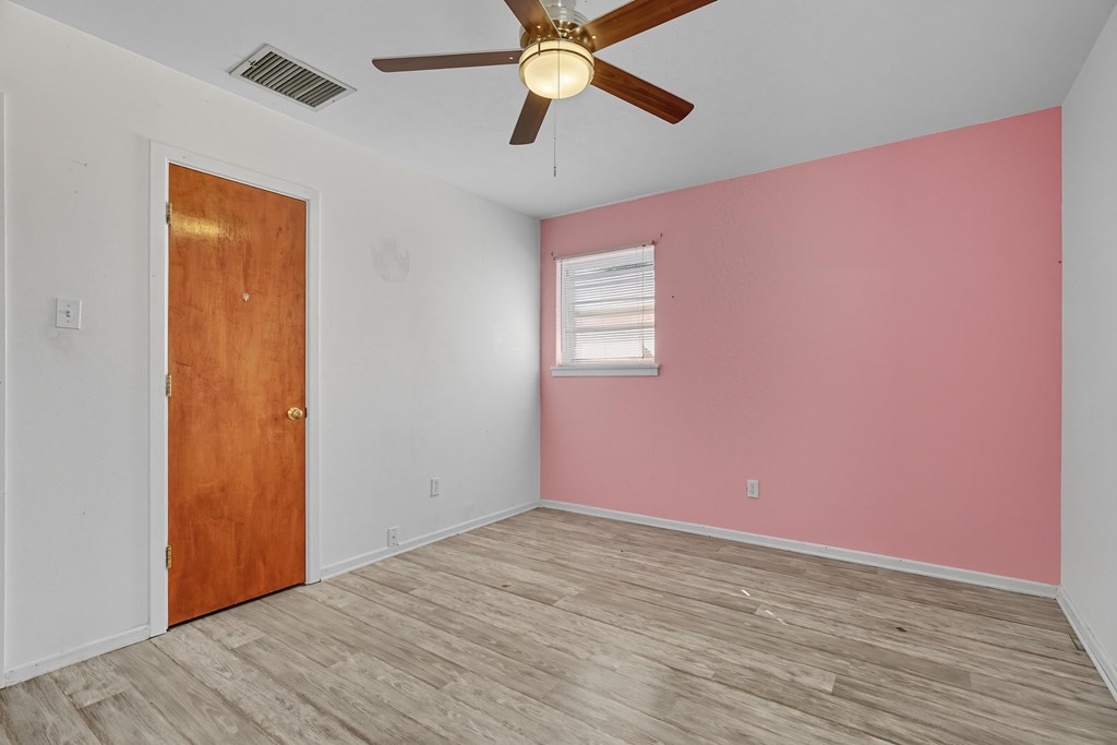 Empty bedroom with a pink accent wall, gray wood-look flooring, and a ceiling fan.