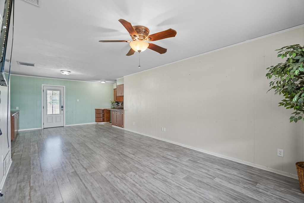 Unfurnished living area with gray plank flooring, ceiling fan, and a compact kitchen.