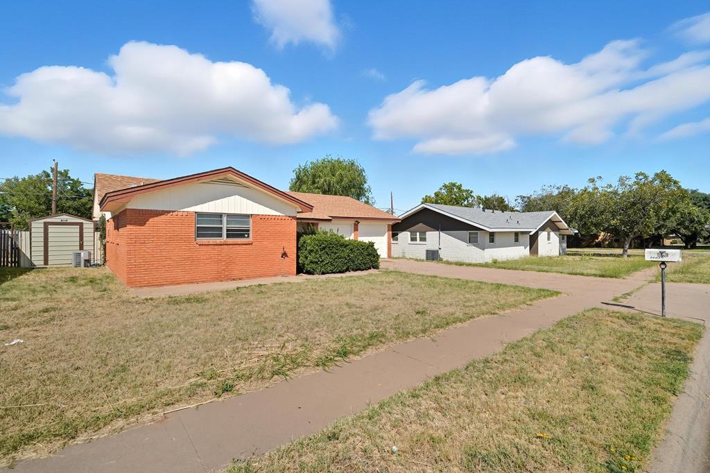 Red brick single-story house with a white gable, dry front lawn, sidewalk, and neighboring homes.