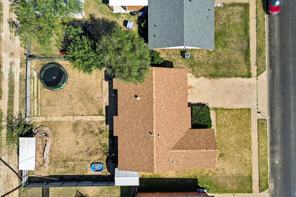 Aerial view of a single-story home with a brown roof, fenced yard, and small blue pool.