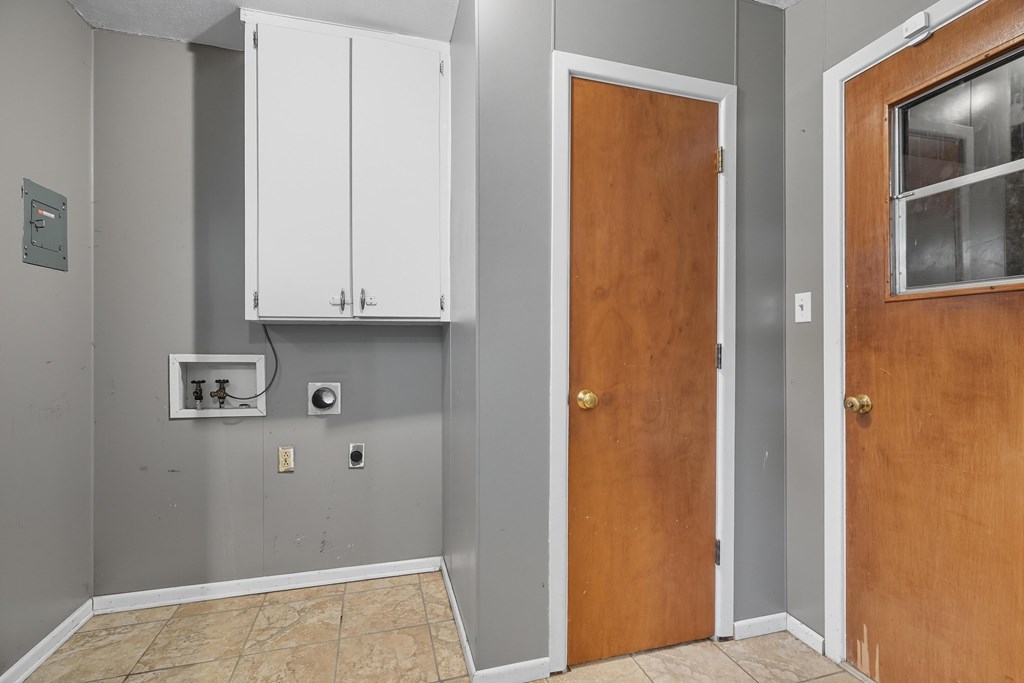 Utility room with washer hookups, a white wall cabinet, and tan tile flooring.