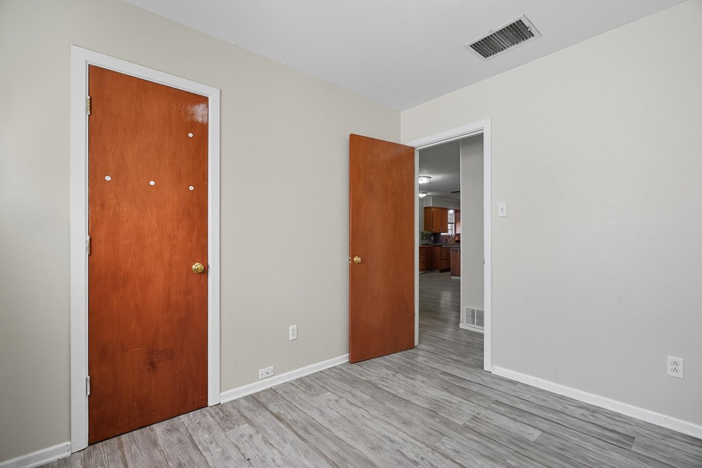 Empty room with gray plank flooring and two wooden doors, opening toward the kitchen.
