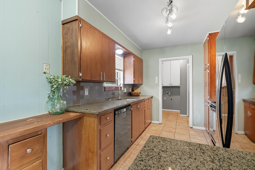 Kitchen with wood cabinets, granite counters, and a narrow tiled walkway.