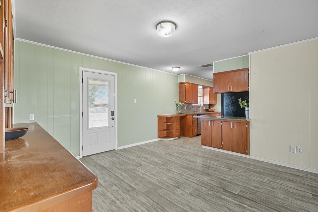 Kitchen and dining area with green paneled walls, warm wood cabinets, and gray plank flooring.