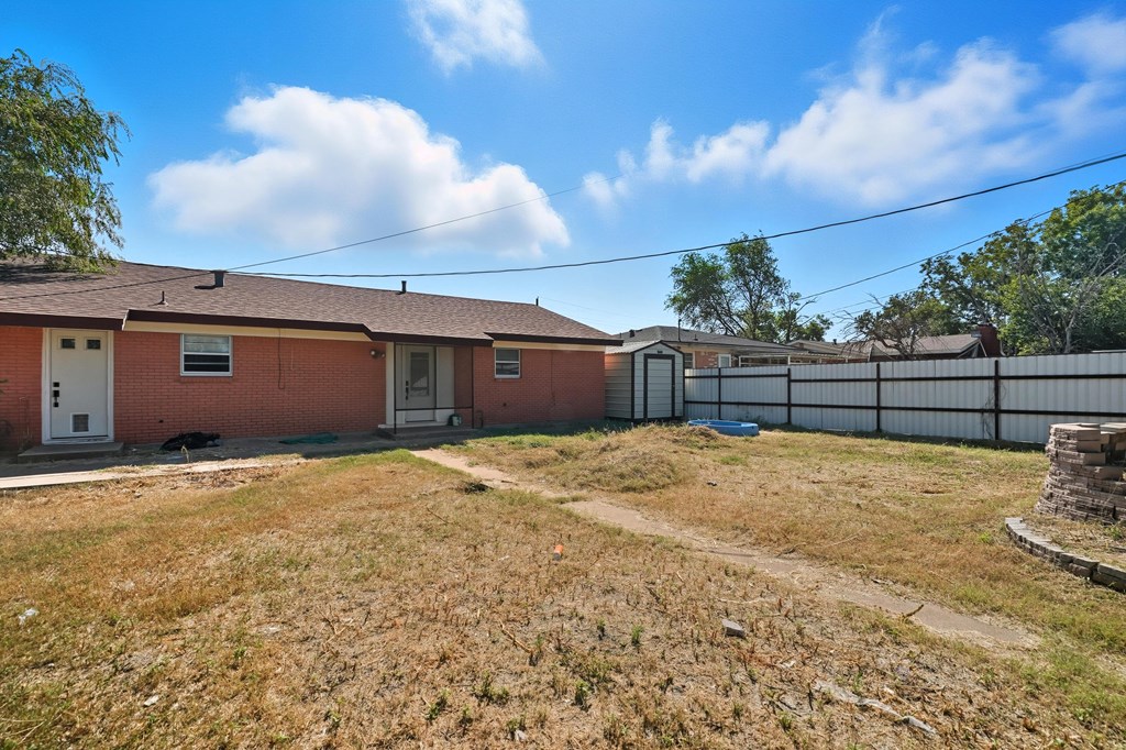 Red-brick home with a dry backyard, white privacy fence, and small shed.