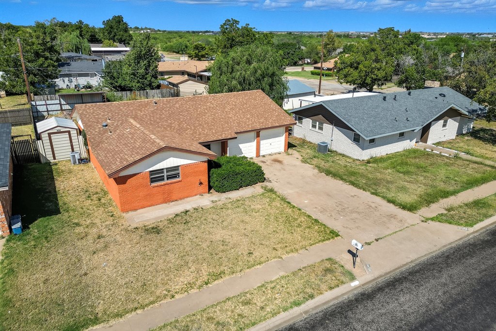 Aerial view of a red-brick house with an attached garage and dry front lawn.