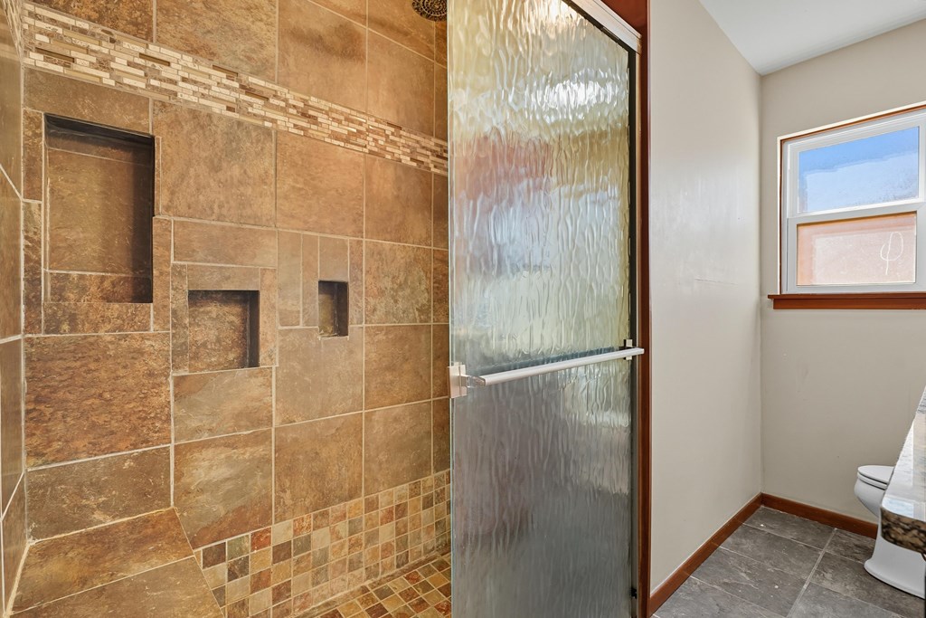 Bathroom with a brown stone-tile shower, mosaic accents, and a textured glass sliding door.