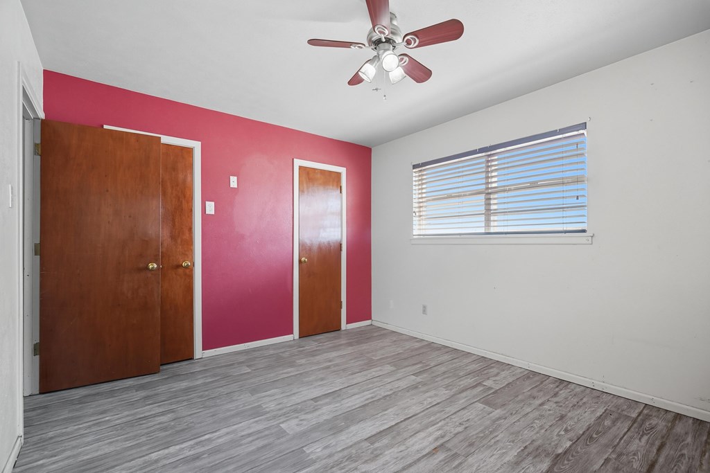Empty bedroom with gray flooring, magenta accent wall, wooden doors, and window blinds.