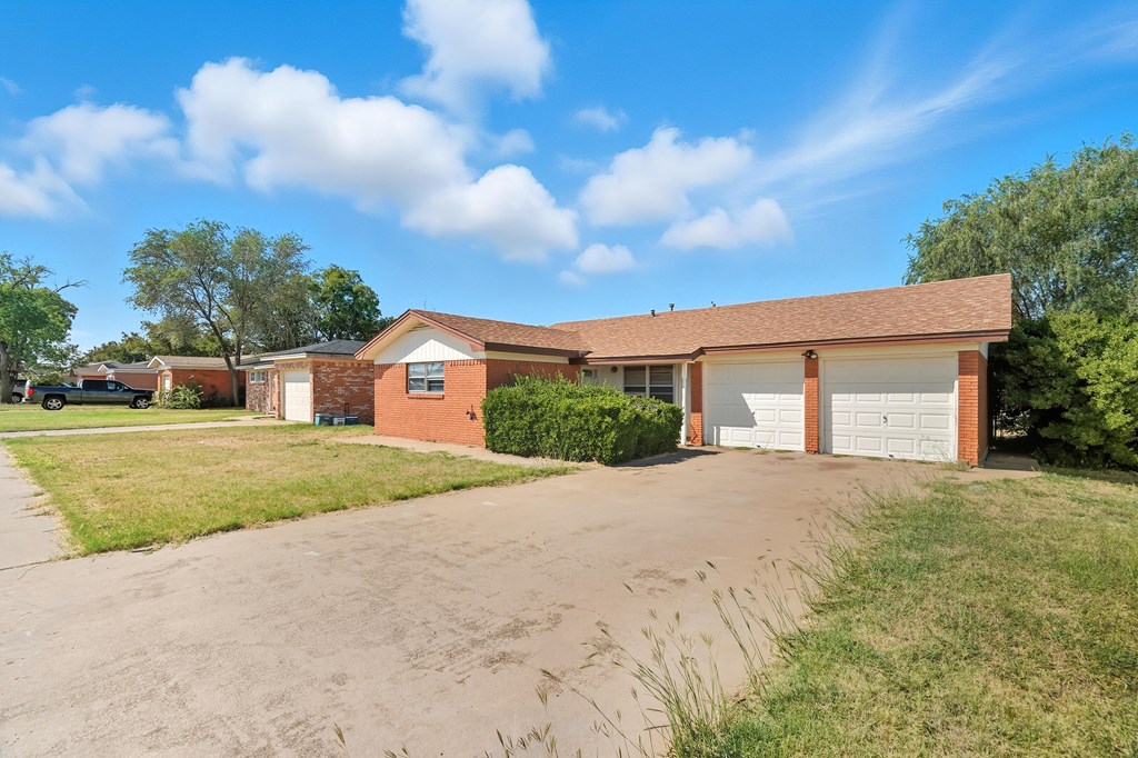 Single-story brick house with two white garage doors and a wide concrete driveway.