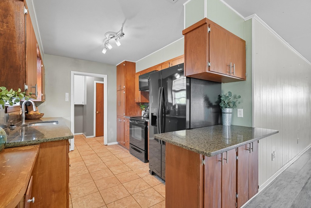 Kitchen with warm wood cabinets, granite counters, and a black refrigerator beside a granite-topped peninsula.