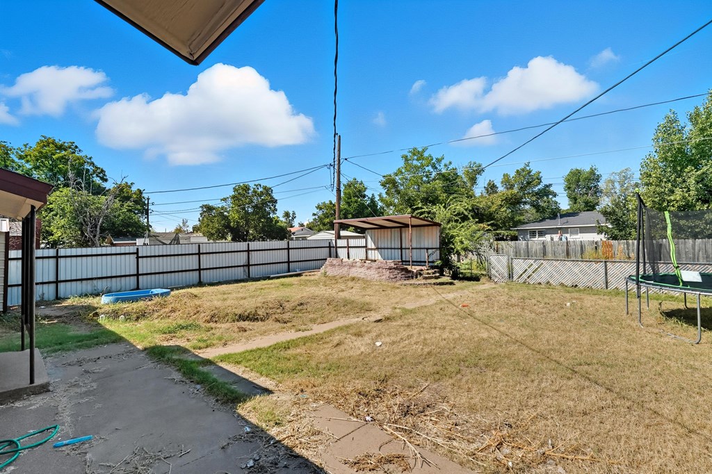 Backyard with a fenced dry lawn, covered patio, small pool, and trampoline.