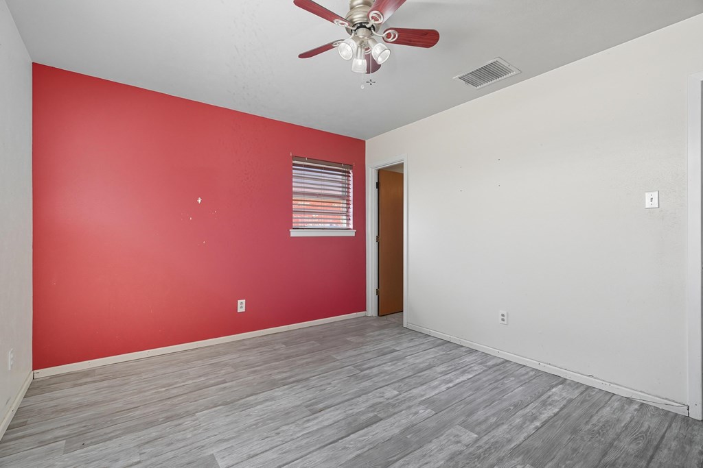 Empty room with a red accent wall, gray plank flooring, and a ceiling fan.