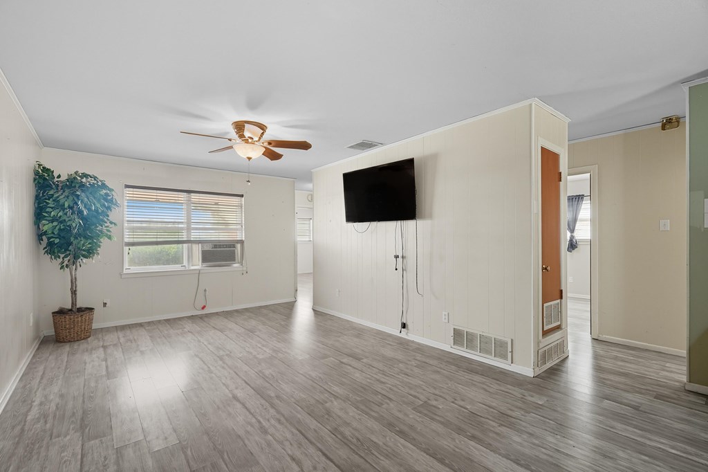 Mostly vacant living room with gray flooring, a wall-mounted TV, ceiling fan, and window air conditioner.