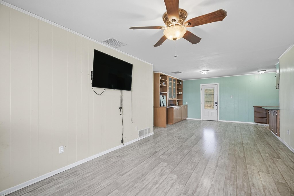 Mostly empty living room with gray wood-look flooring, built-in shelves, and a ceiling fan.