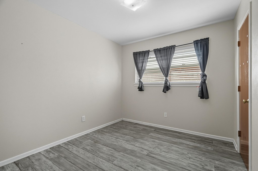 Empty room with gray plank flooring and a curtained window.