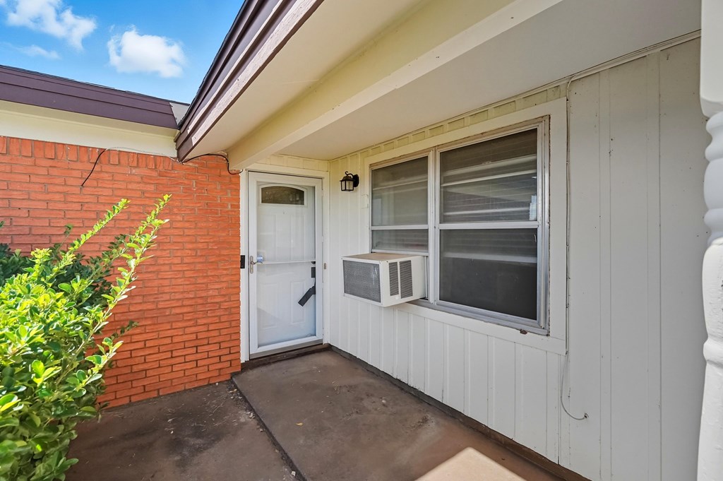 Home entrance with a white door, red brick wall, and window-mounted air conditioner.