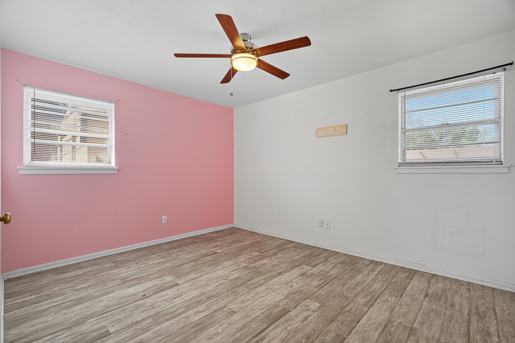 Empty bedroom with a pink accent wall, wood-look flooring, and a ceiling fan.