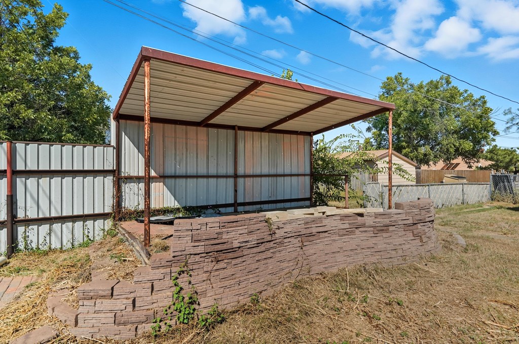 Backyard covered patio with a metal roof and curved low brick wall.