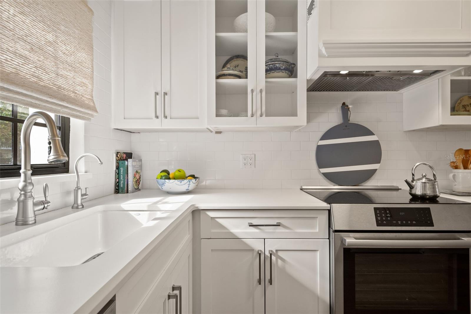 White kitchen with a farmhouse sink, glass-front cabinets, and stainless steel range.