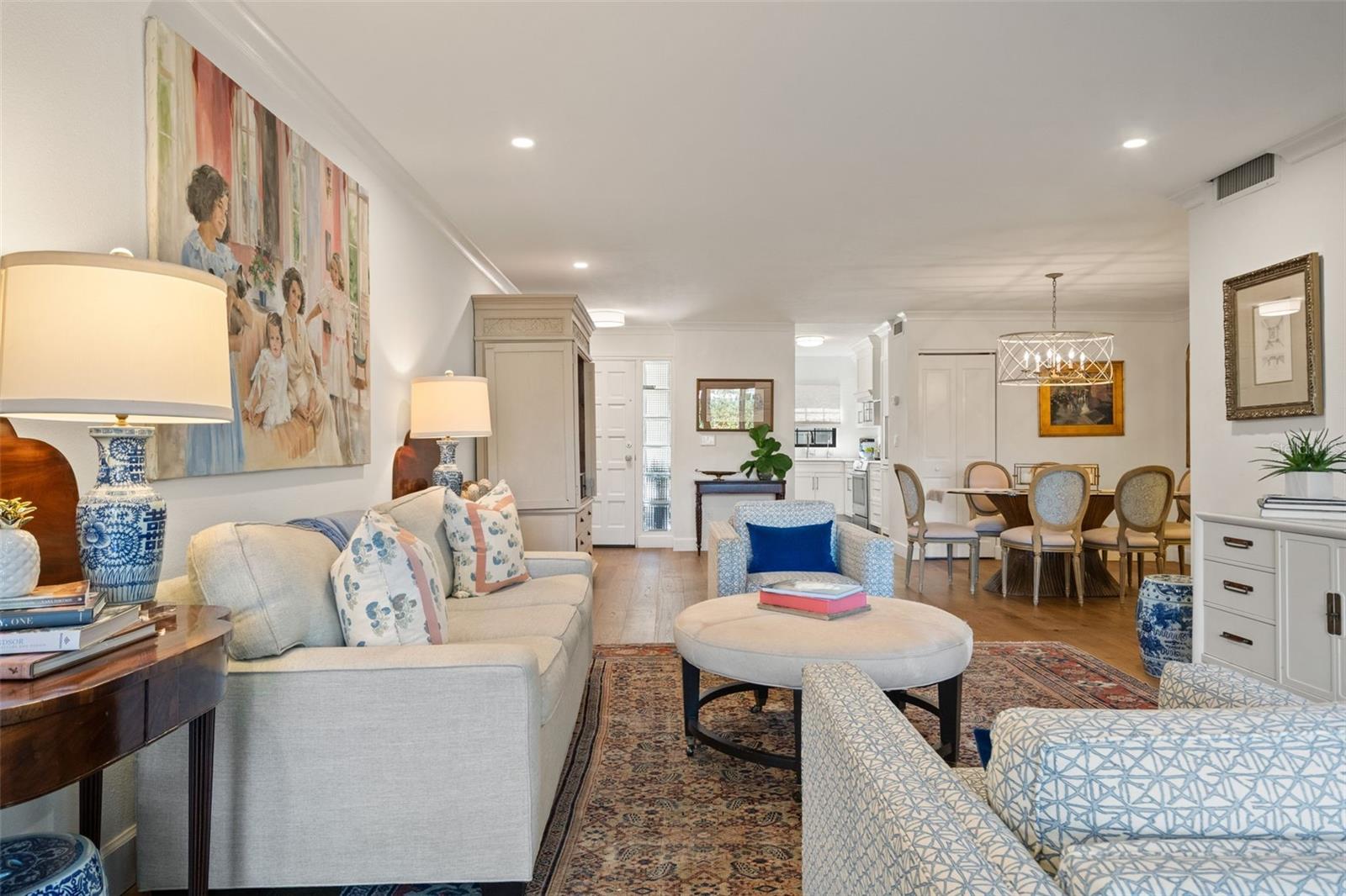Living room with pale sofas and patterned rugs, opening to a dining area and kitchen.